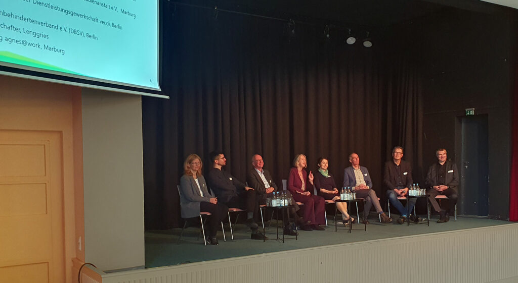 Foto: Die Teilnehmer der Podiumsdiskussion sitzen in einer Reihe auf der Bühne.